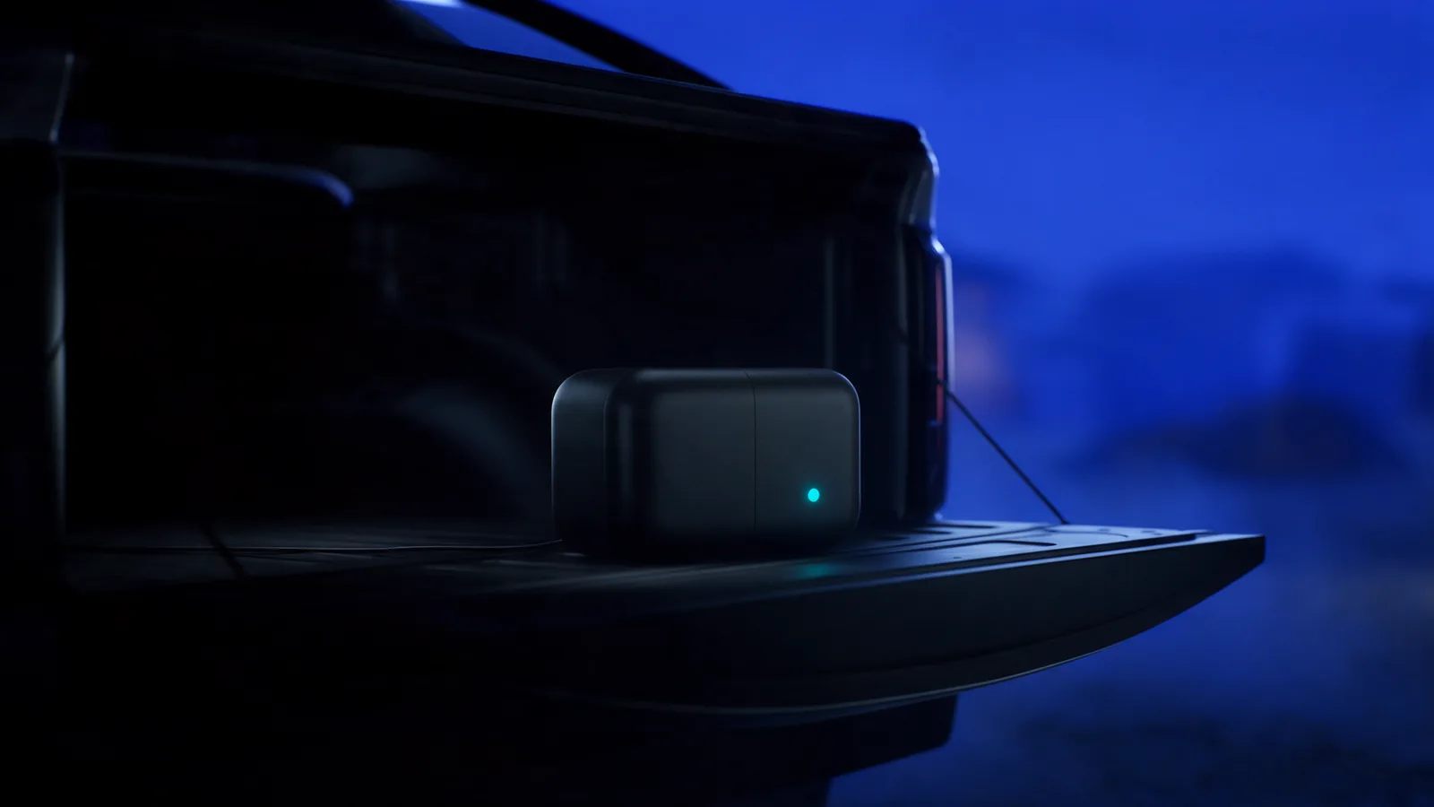 The same sealed unit on an open tailgate at night, drawing power from the vehicle, its status light the only bright point.